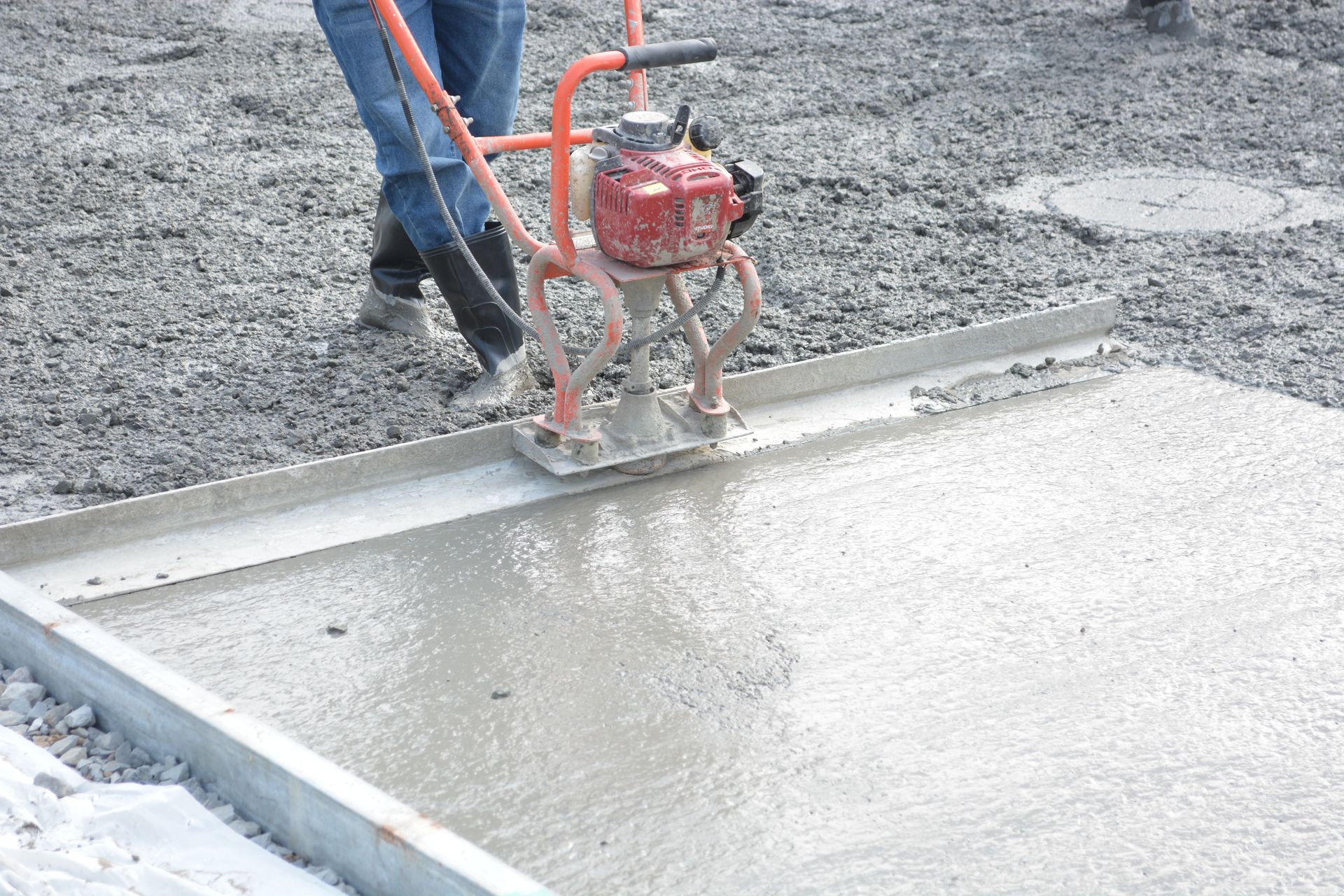 A construction worker operates a power trowel to smooth freshly poured concrete on a construction site.